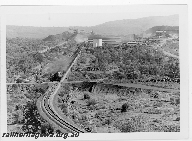 P19221
Mount Newman Mining (MNM) Locotrol train - 270 cars departs Newman mine site. Mine site in background.
