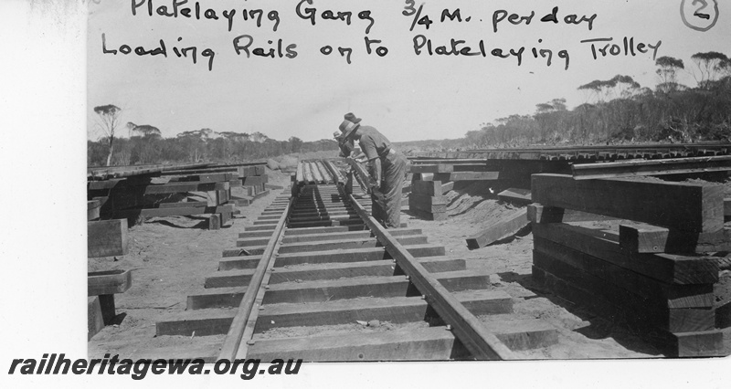 P19661
Plate laying gang - loading rails on to plate laying trolley. Location unknown.

