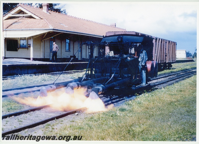 P20059
Woolery weed burner, in operation on track, operator, station building, platform, onlooker, Tambellup, GSR line, front and side view
