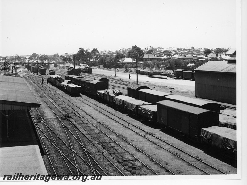 P20072
Northam station and yard, looking east from signal box, platform, canopy, sidings, rakes of goods wagons and vans, bracket signals, pedestrian overpass, goods shed, loading ramp, fixed crane, houses, ER line, view from elevated position
