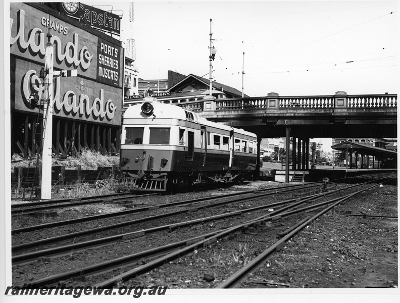 P20113
Governor class railcar, signal, advertisements for Orlando, Capstan, and Milnes Whisky, road bridge, platform, canopy, Perth city station, front and side view 
