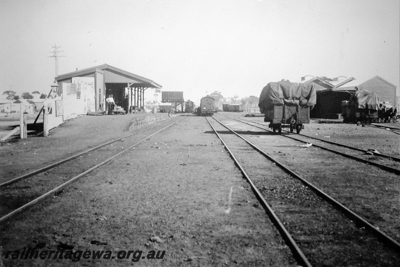 P20793
Kellerberrin station and yard looking west. Wagons in foreground,  steam locomotive taking water in rear of photo. 1st class goods shed on right of photo.  EGR line.
