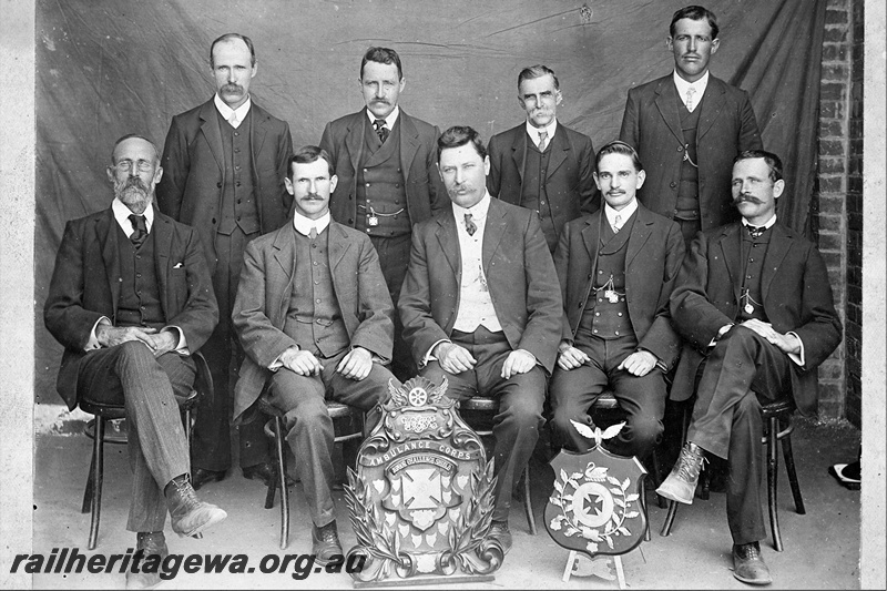 P21182
Group photo of 9 men displaying Ambulance Corps Junior Challenge Shield, and another smaller shield with Maltese cross and swan

