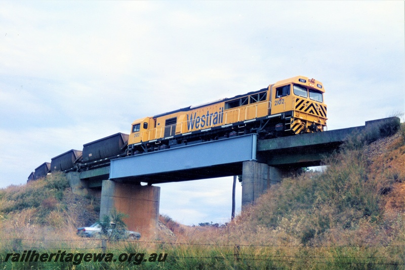 P21356
Westrail S class 2102 loco in the yellow with black chevrons livery heading a loaded bauxite train  over the bridge spanning the South West Highway near Mundijong, view of the train looking upwards on the bridge.. 
