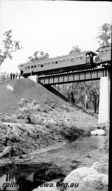P22905
Commissioner's Tour train, stopped on concrete and steel bridge, river, four men standing on tracks, view from riverbank
