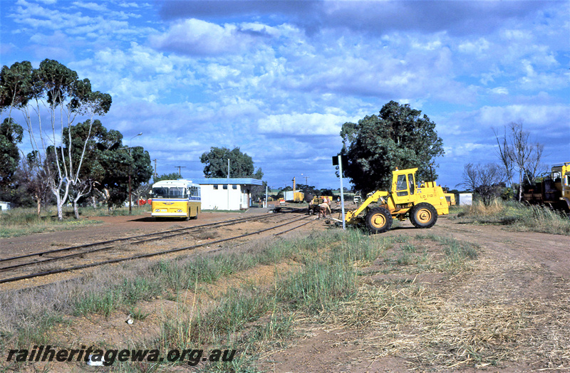 P23048
Front end loader, workers, bus, buildings, tracks, siding, trees, Carnamah, MR line, long view from trackside
