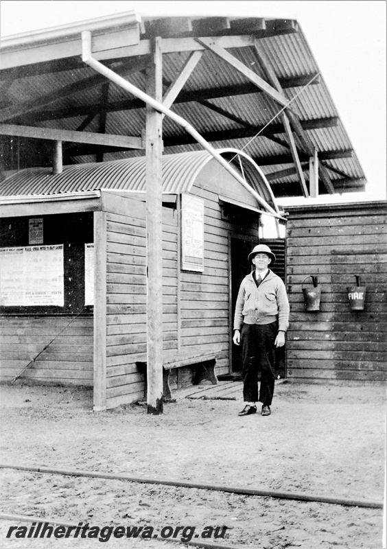 P23111
Station buildings under an overall roof, fire buckets hanging on a shed wall, employee wearing a pith helmet, Wokarina, GA line
