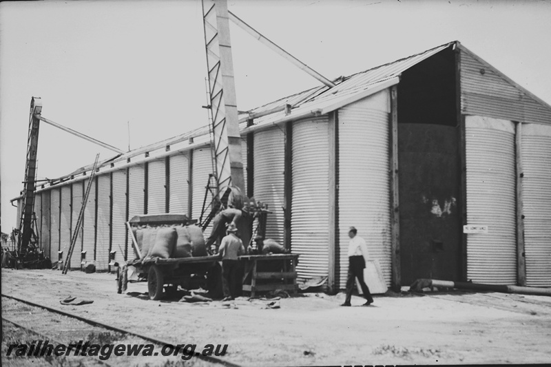 P23172
Wheat bin, grain loaders, truck, wheat bags, workers, side and end view of building from ground level 
