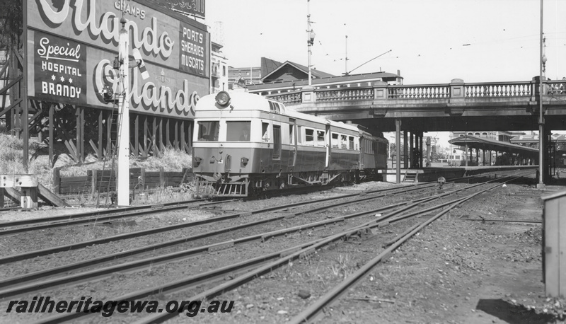 P23249
ADE class 449 Governor Weld with AL class carriage as trailer departing Perth for Katanning passing under Barrack Street bridge in front of the hoarding advertising Orlando Ports,  Sherries and Muscats, tram passing over Barrack Street bridge, another ADE class in the dock, ER line. See also P00652, P20113
