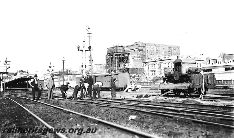 P23298
Gangers working on the track near Perth Station with compressor mounted on a H wagon. In the background is the General Post office, water tank and Fremantle dock platform with D class locomotive waiting to depart. ER line
