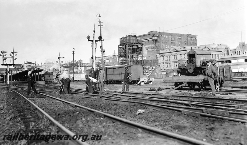 P23299
Gangers working on the track near Perth Station with compressor mounted on a H wagon. In the background is the General Post office, water tank and Fremantle dock platform. ER line
