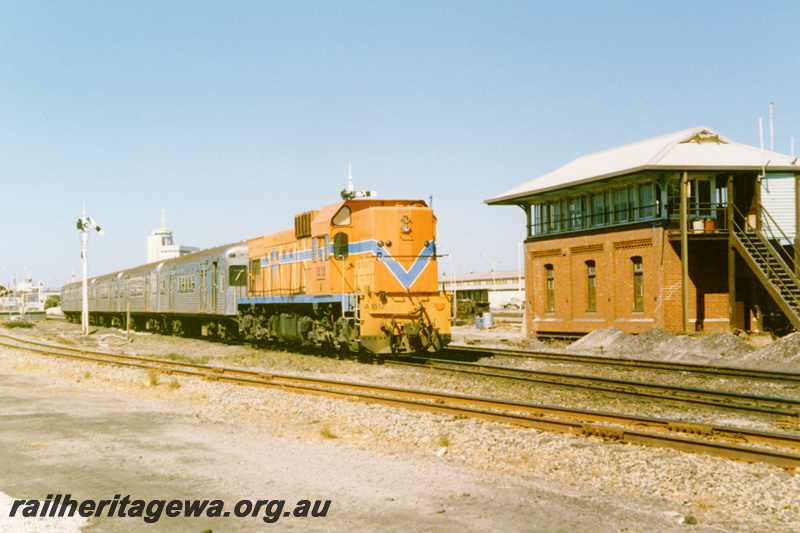 P23355
A class 1512 in the Westrail orange with blue stripe livery hauling a train of the Queensland suburban carriages, signal, signal cabin Box B,, train departing Fremantle, ER line, view along the train..
