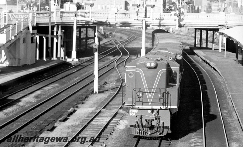 P23949
RA class 1918 on goods train, platforms, canopy, ramp, bracket signals, road bridge, city buildings, Perth station, ER line, front view from elevated position
