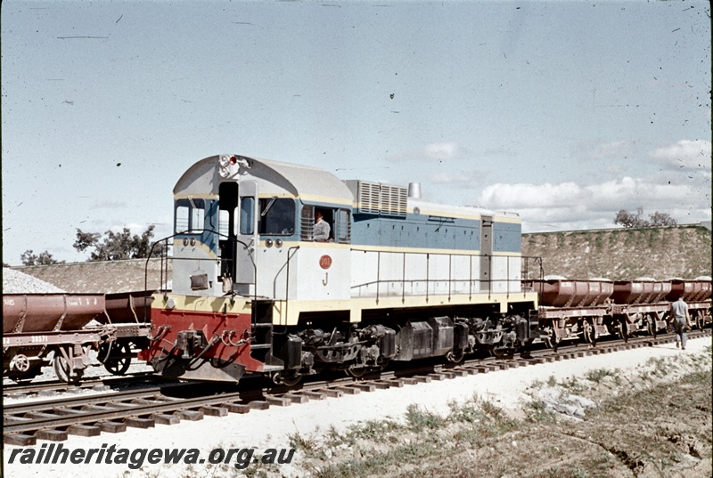 T04646
J class 101 standard gauge diesel locomotive at the head of a ballast train of 4 wheeled wagons at Kenwick with loaded wagons on an adjacent line.
