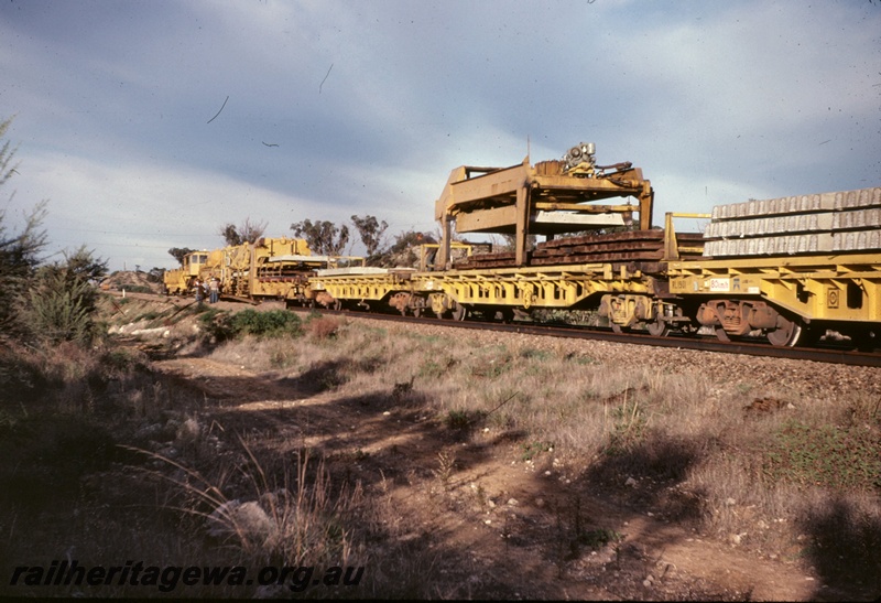 T05091
Track replacement machine P811, RL class flat wagon 1901, on works train, near Cockburn Street, Kalgoorlie to Kwinana Rehabilitation Project, view along side of train towards the front
