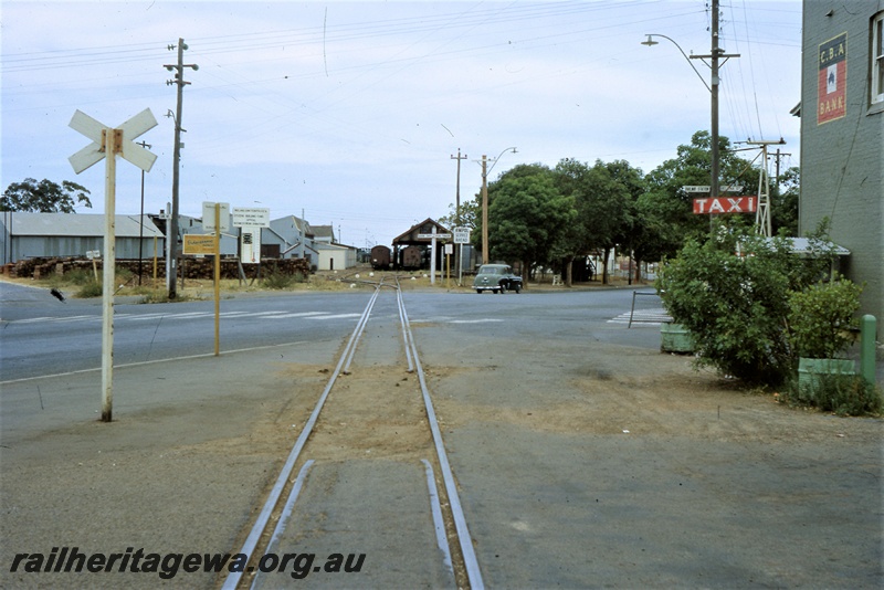 T05437
Rail track crossing Great Eastern Highway, rail crossing sign, industrial buildings, motor car, Midland Railway Co. (MRWA) yard, carriage shed, sidings, points, Midland, MR line, view at road level  across road from Tuhoy Gardens into the yard
