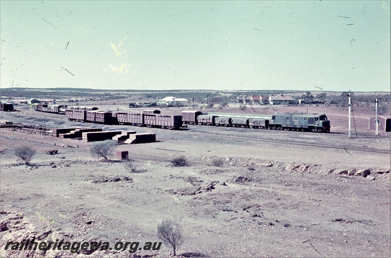 T05456
X class diesel, on goods train, arriving at yard from the south, signals, rakes of wagons and vans, houses in background, Mullewa, EM line, side and front view taken from coal stage
