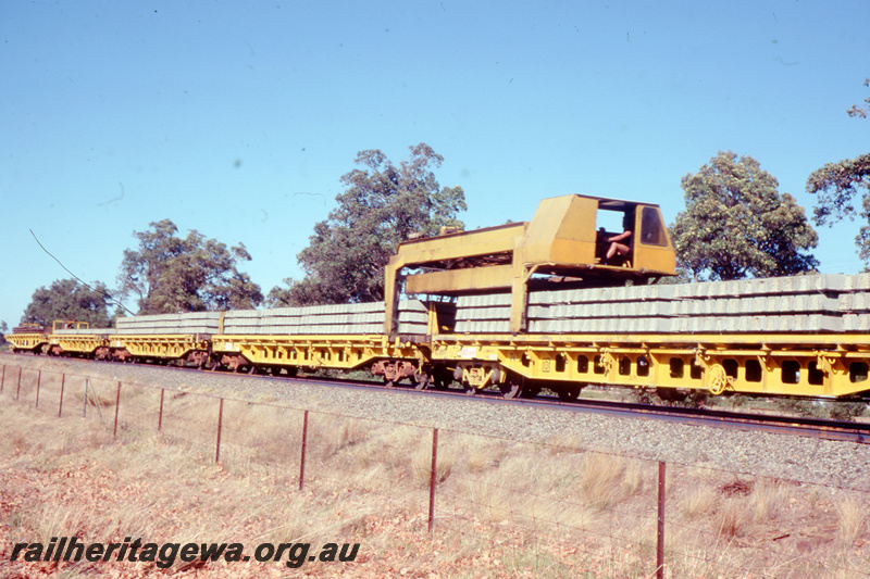 T05783
3 of 8 views of the work on the Kalgoorlie to Kwinana Rehabilitation Project featuring the P811 Track Replacement Machine. Five flat wagons carrying concrete sleepers with the removal apparatus over one of the wagons.
