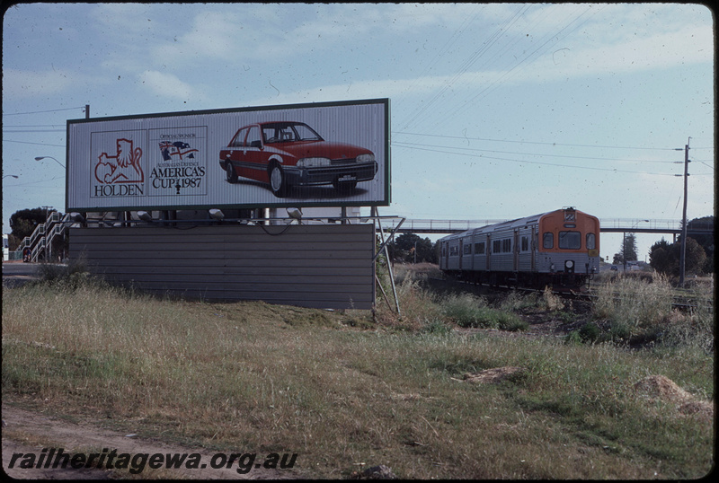 T08277
ADL/ADC Class railcar set, Up suburban passenger service, between Cottesloe and Mosman Park, billboard advertising the Holden Commodore and America's Cup, footbridge, ER line
